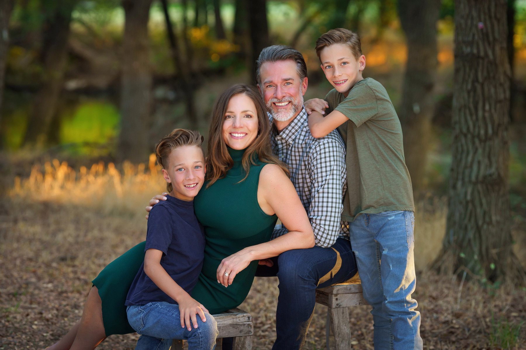Family of four seated together in the woods at golden hour