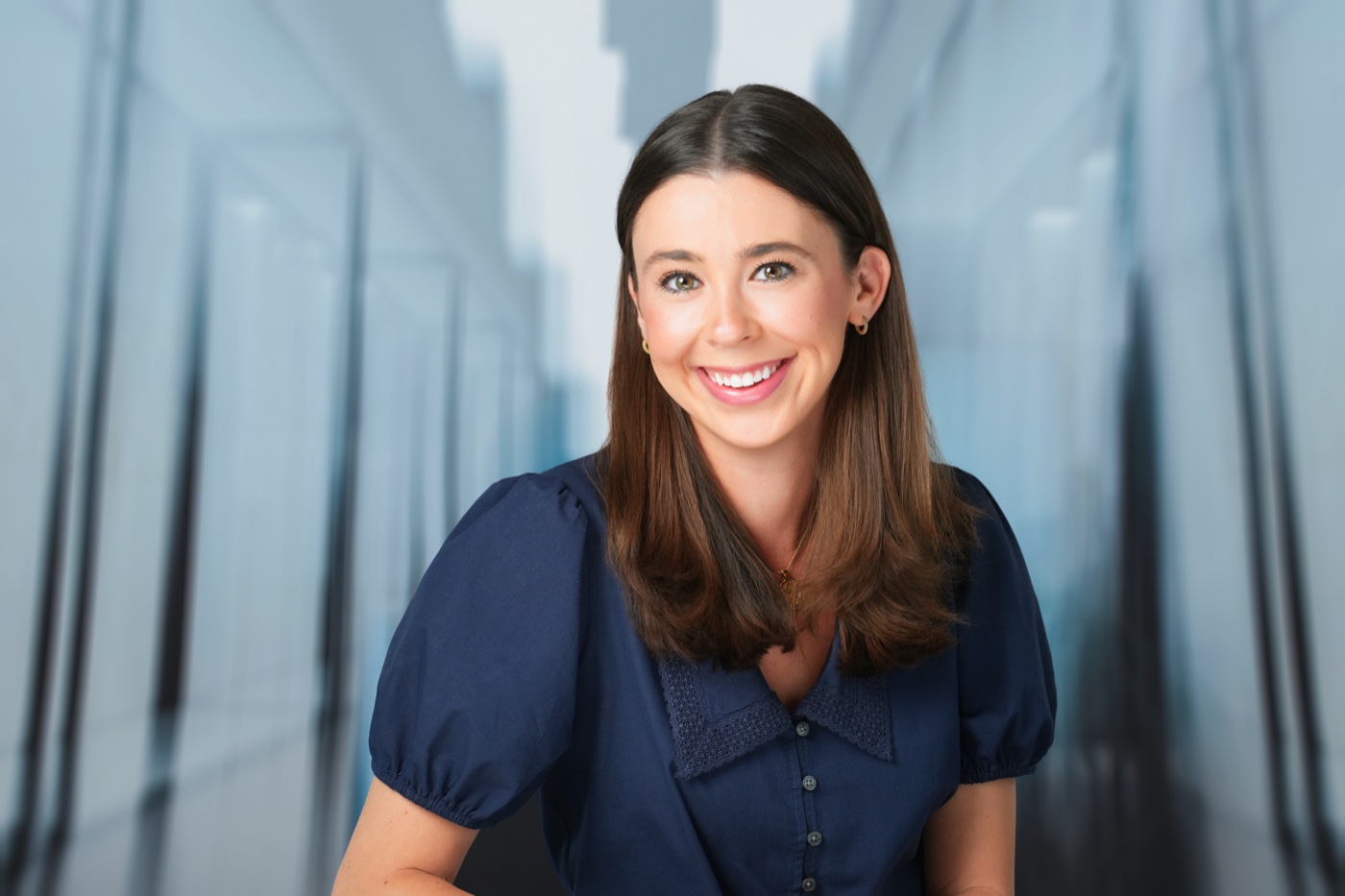 Studio headshot of a woman in a navy blouse with a blue city office background added