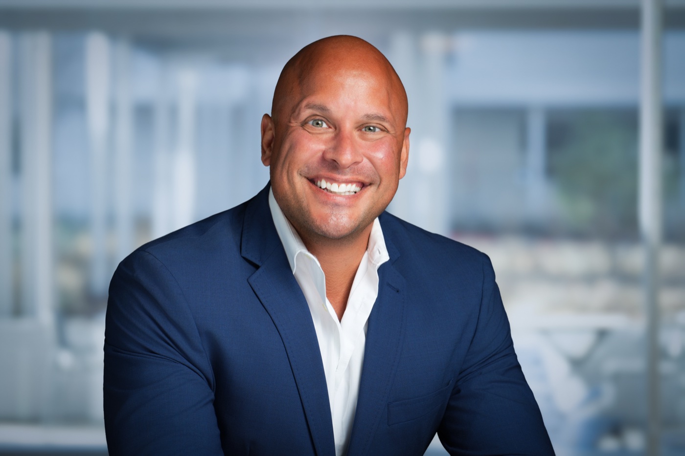 Studio headshot of a man in a navy blazer with a glass-walled office background added