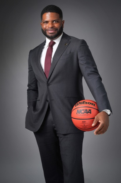 Studio portrait of a man in a charcoal suit holding a basketball