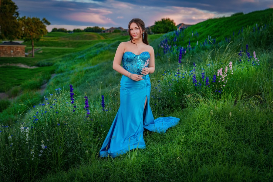 High school senior in a blue gown photographed among bluebonnets at sunset
