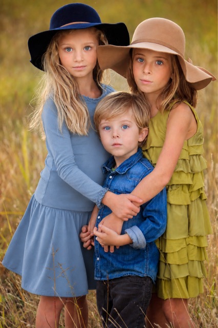 Three children standing together in a field of tall grass at golden hour