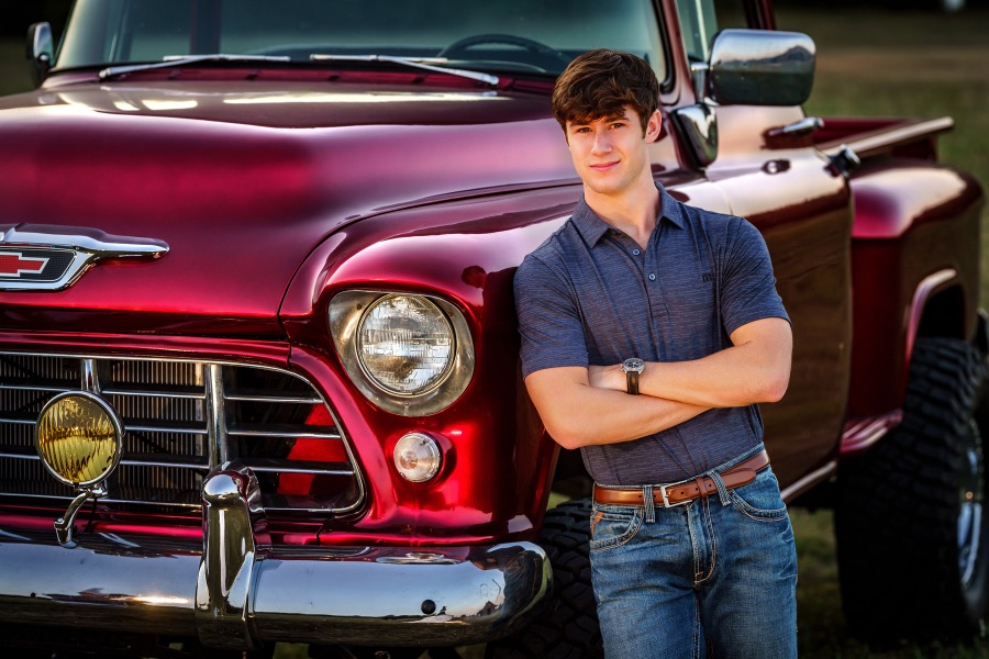 High school senior photographed on location beside a classic red pickup truck